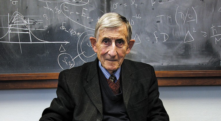 Freeman Dyson sits in front of a blackboard covered in mathematical notation
