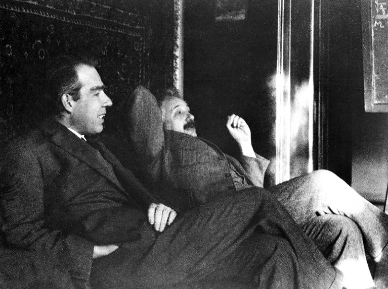 Black and white photo showing Bohr and Einstein sitting side by side in conversation.
