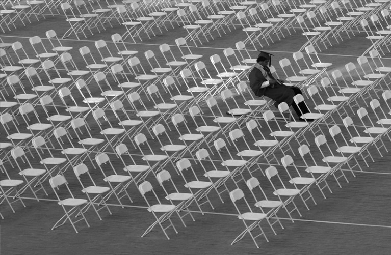Graduate sits alone in rows of white chairs