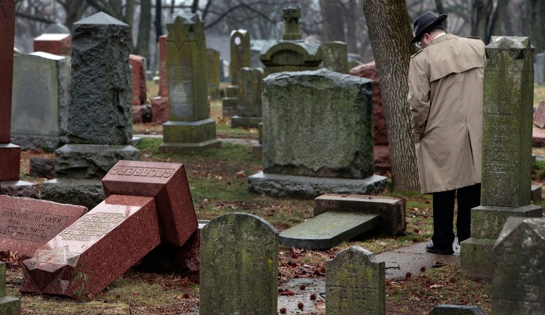 A passer-by looks at topped gravestones in a Jewish cemetary