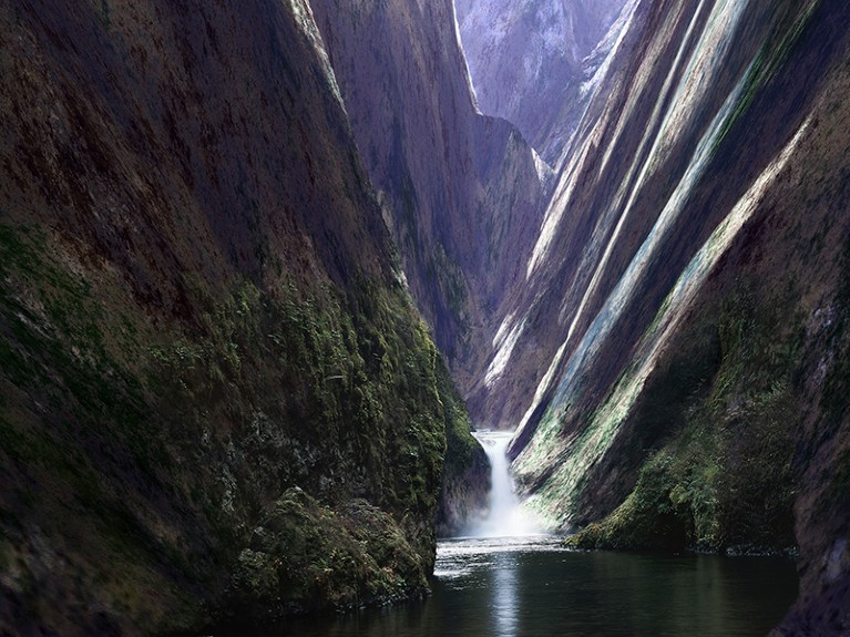 A narrow river runs between steep mountains, with a waterfall.