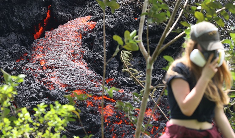 A local resident in a dust mask passes a lava flow from a new fissure following recent eruptions of Kilauea Volcano in Hawaii.
