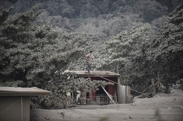 A man gazes at the camera while standing on a roof in the ash-covered village of San Miguel Los Lotes near Guatemala on 4.6.18