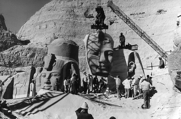 Worken lift the faces of huge statues on cranes in this black and white photograph from Abu Simbel.