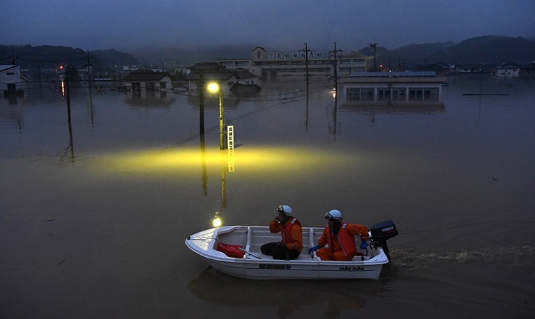 Fire fighters power their boat past a submerged streetlight at night on July 7th in Kurashiki, Japan