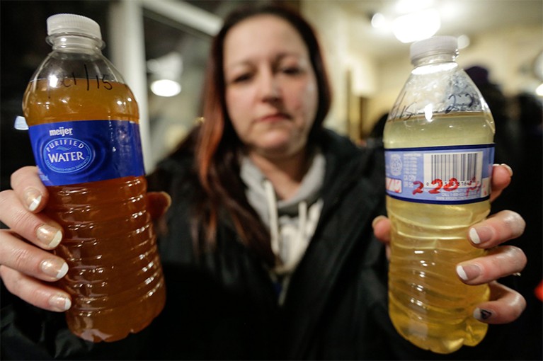 LeeAnne Walters holds two bottles of dirty water, one brown one yellow, that she took from her home to show officials.