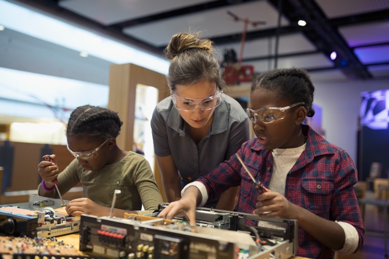Scientist watching two girls assembling electronics