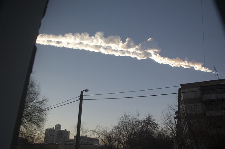 A billowing contrail across a blue sky, seen in between two buildings in Russia.