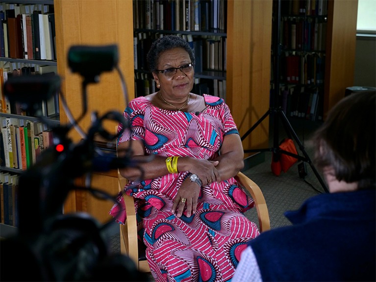 Asomoah-Hassan, wearing a pink printed dress, looks to Schmitt (off camera) while being interviewed for his film 'Paywall'