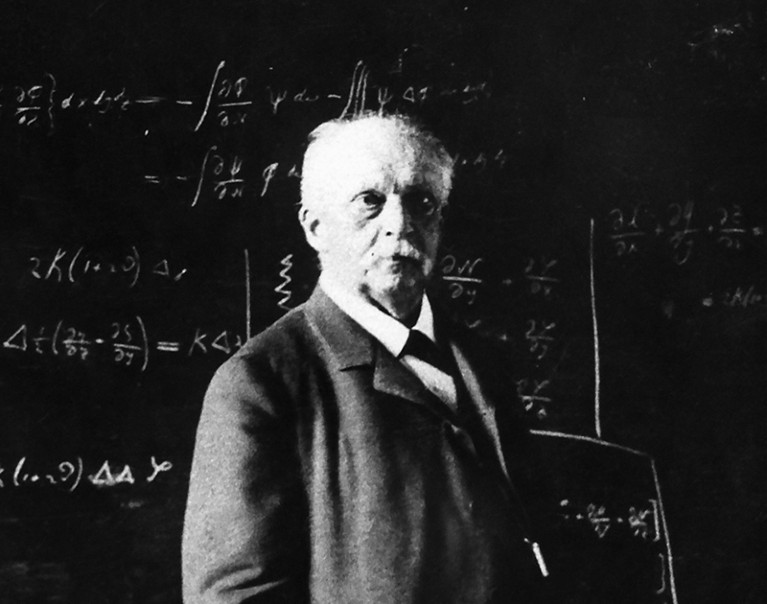 Hermann Helmholtz, suited in front of a whiteboard covered in equations, gazing off camera.