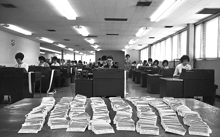 Rows of mostly women working in a Standard Oil office. A stack of Standard Oil credit cards sit on the table at front