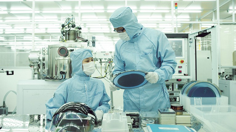 two researchers looking at silicon device in clean room at DGIST