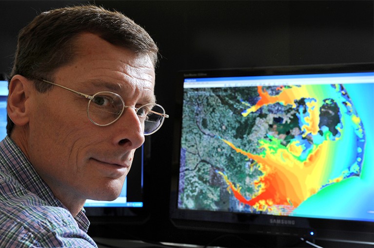 Dr Richard Luettich. Behind him a screen is shown with a computer model for predicting storm surges.