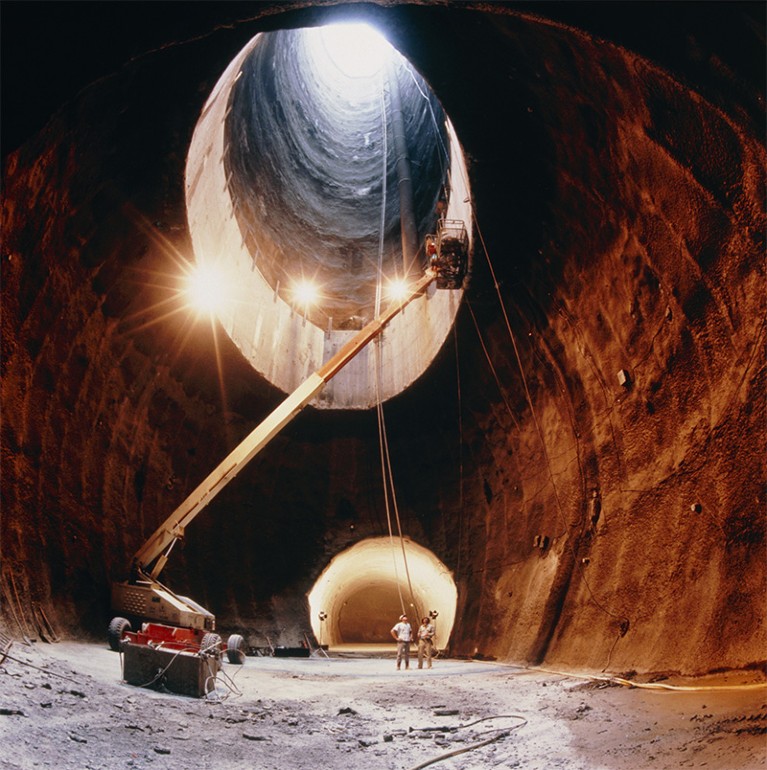 A crane (l) can be seen working on the delivery shaft of the SSC. Two men stand pointing in front of the lower ring tunnel