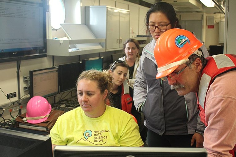 Marine biologist Kelly Robinson sits at a computer while members of her team look over her shoulder at the screen