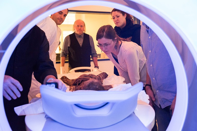 Five Researchers look at a mummy as it enters a CT machine for scanning.