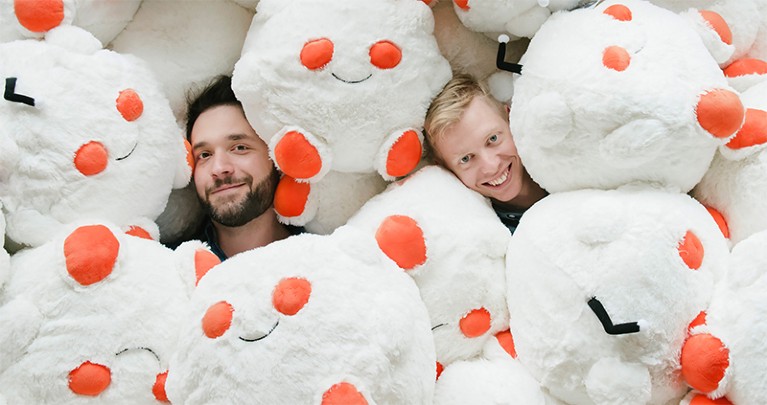 Ohanian (l) and Huffman (r) smile up from under a pile of Reddit-logo-shaped soft toys
