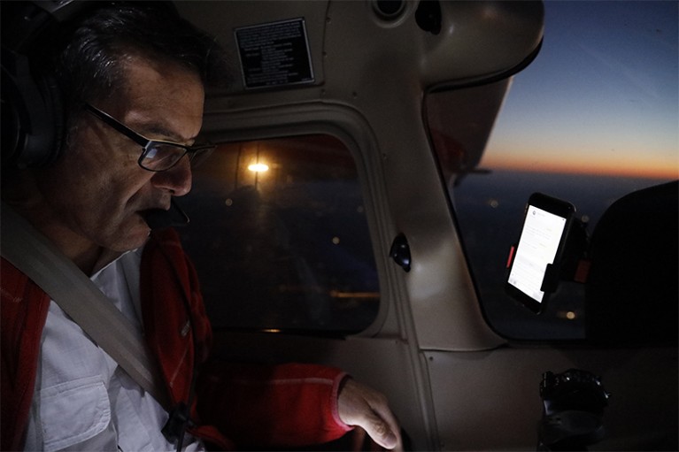 Wikelski(左)低头看着塞斯纳飞机座舱里的跟踪监视器。透过窗户可以看到日落。