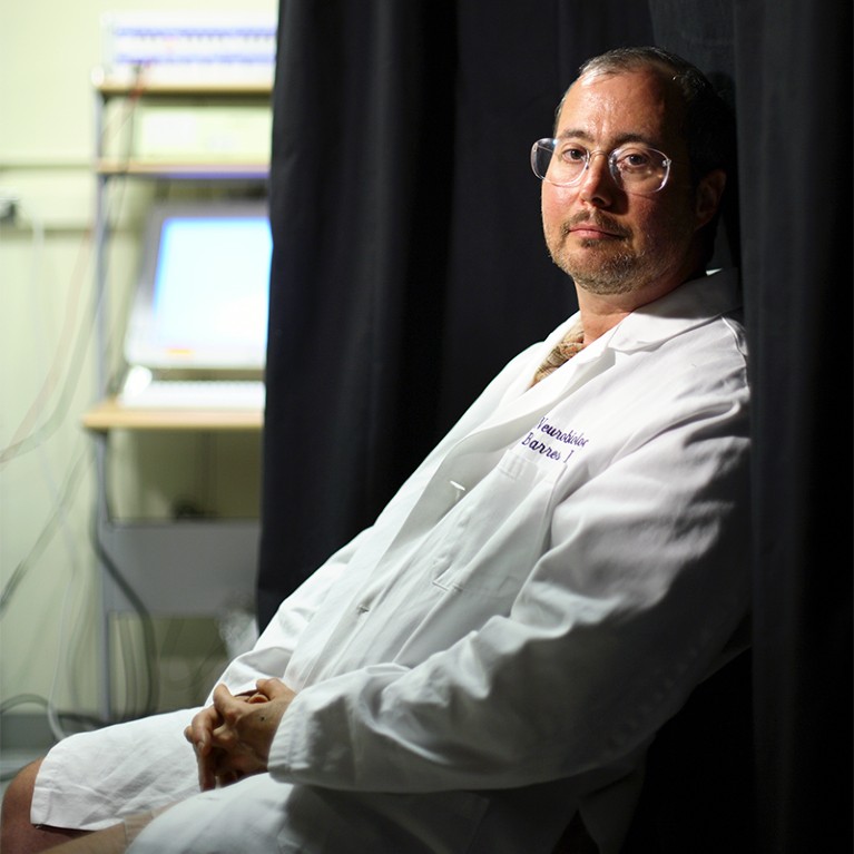 Ben Barres, seated in a lab coat, gazes out towards the camera.