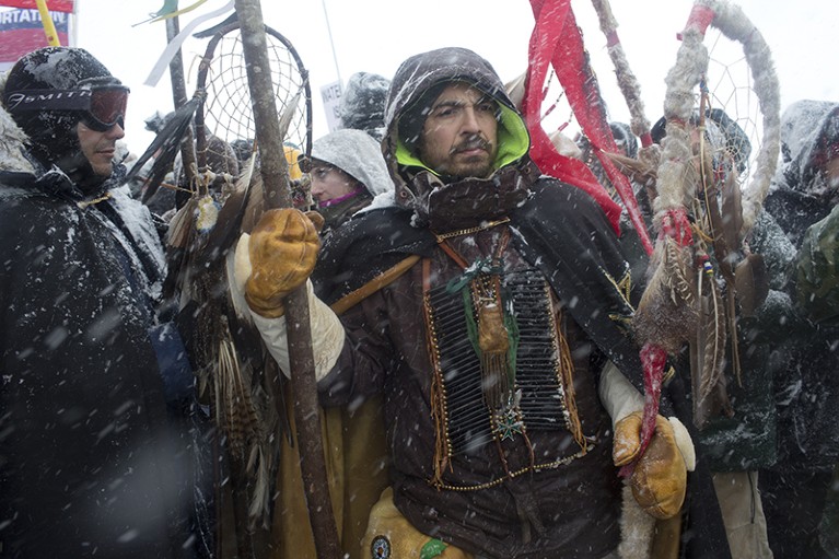People hold totems and flags in snowy weather as they defend theStanding Rock protest camp on December 5th 2016