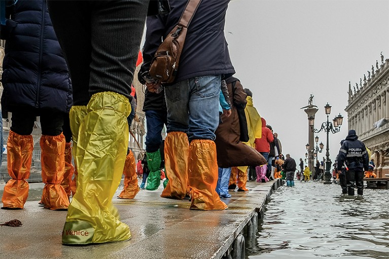 Tourists in colourful waterproofs walk across an emergency wooden boardwalk in St. Mark's Square in Venice to avoid floodwater