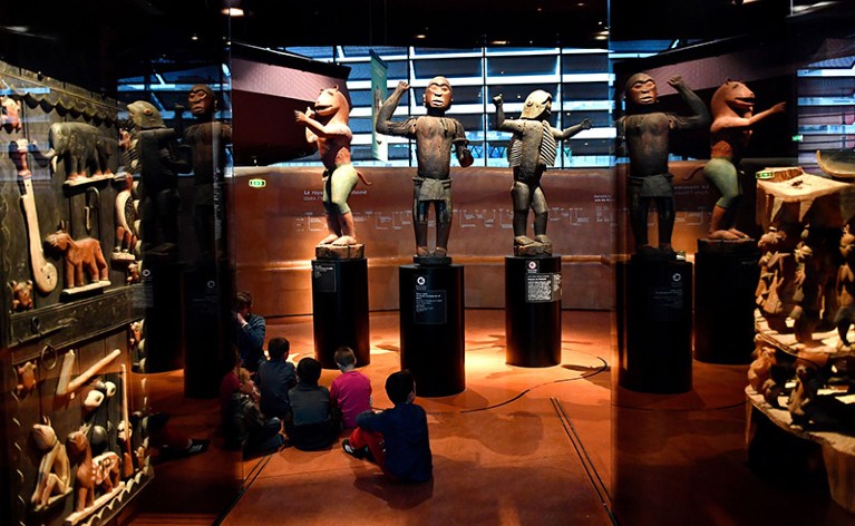 African statues on plinths in a Parisian museum, children sit on the floor looking at the exhibit.