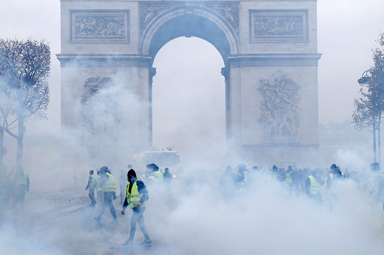 Protesters wearing yellow vests walk among tear gas
