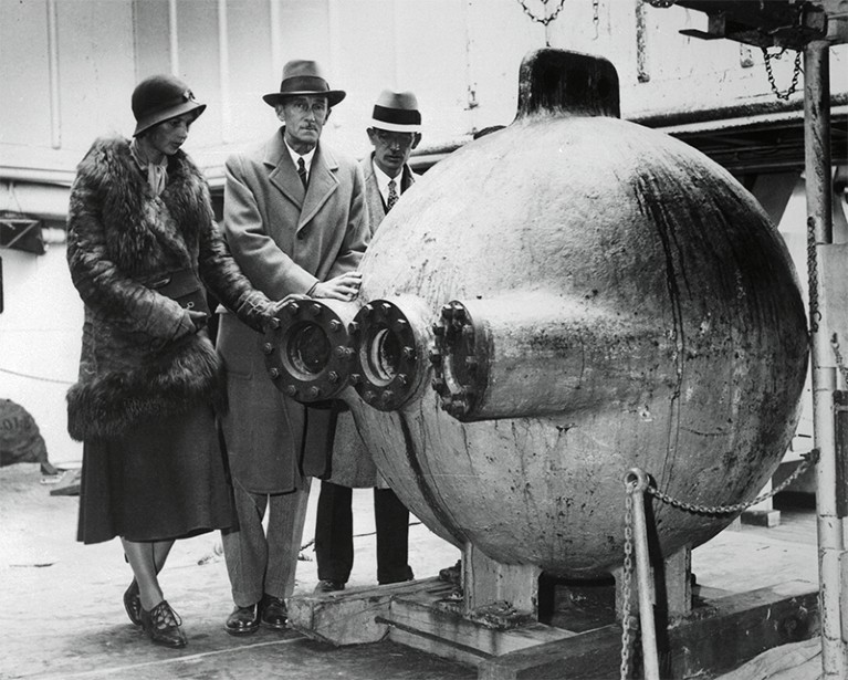 Photograph of Gloria Hollister, William Beebe and John Tee-Van standing around their bathysphere