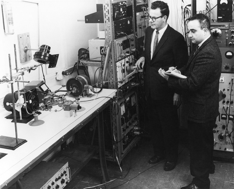 Black and white photo of US physicist Gordon Gould (c) and Ben Senitsky (r) workingwith masers at TRG labs in the 1950s.