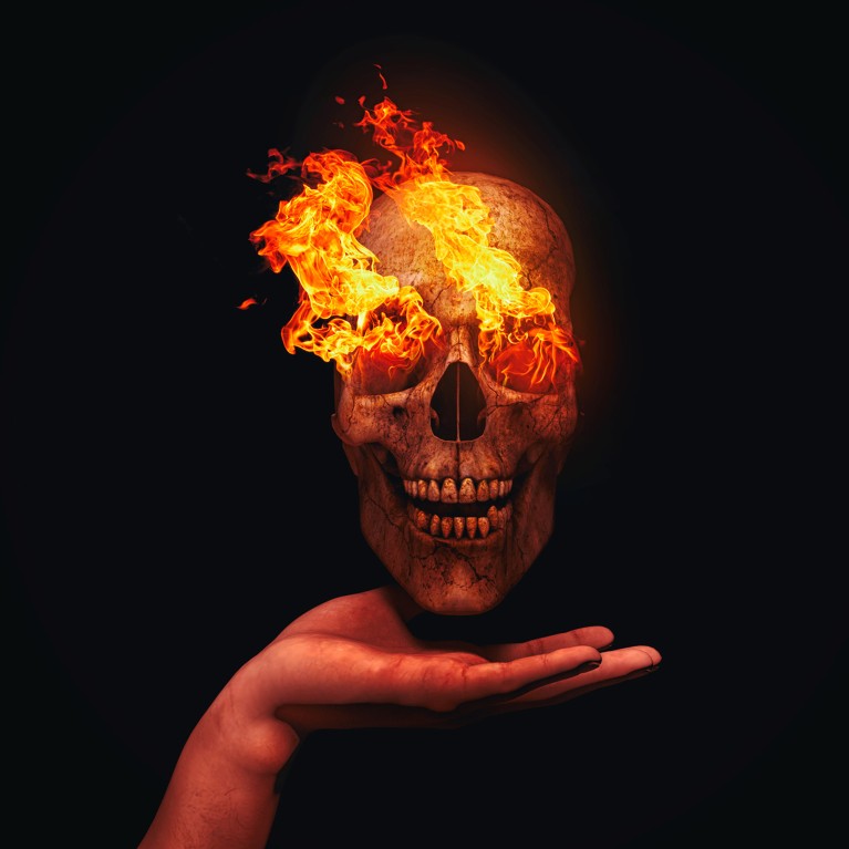 Artistic image of a flaming human skull held in the palm of a human hand