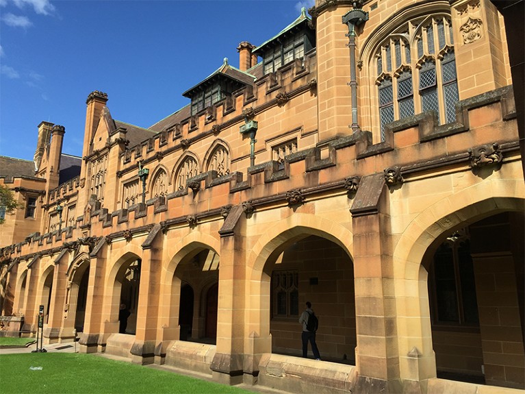 A student walks in the shadows of the Quadrangle arches at the University of Sydney