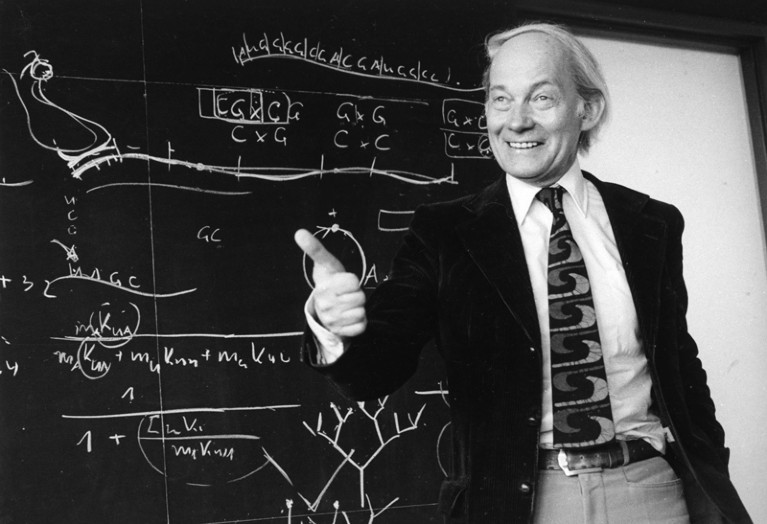 Manfred Eigen standing in front of a blackboard during a lecture in 1979