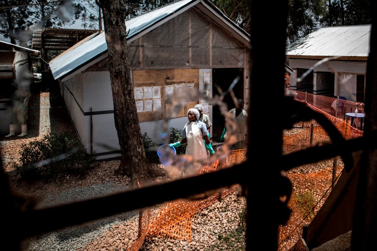 Health workers seen through a bullet hole left in the window of an Ebola treatment centre in the Democratic Republic of Congo