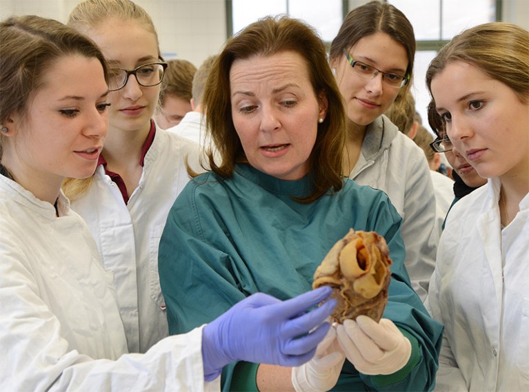 Heike Kielstein is surrounded by students and holds a model of the heart.