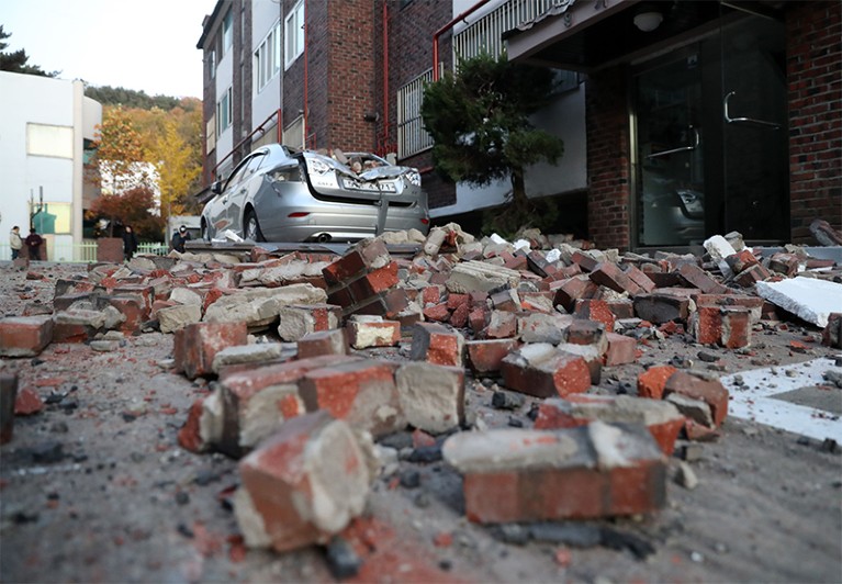 Bricks and debris from damaged buildings lie on the ground in front of a damaged car in Pohang, South Korea