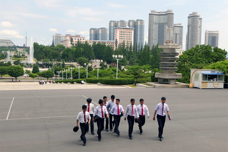 Students walk across Kim Il-sung Square with Pyongyang city in the background.