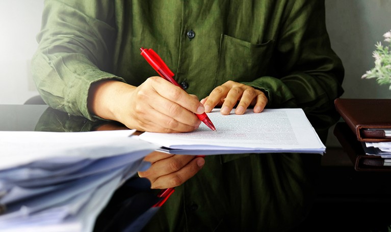 A Hand holding a red pen writing on white paper.