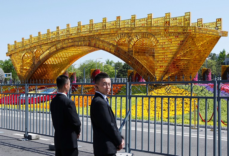 Security personnel stand guard near a "Golden Bridge on Silk Road" decoration for the Belt and Road Forum in Beijing, China