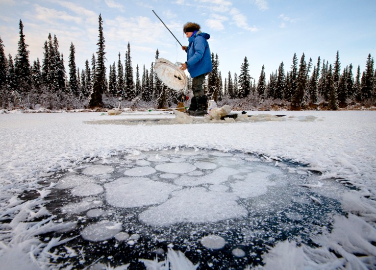 A scientist conducts research on a frozen lake with methane collecting beneath the ice