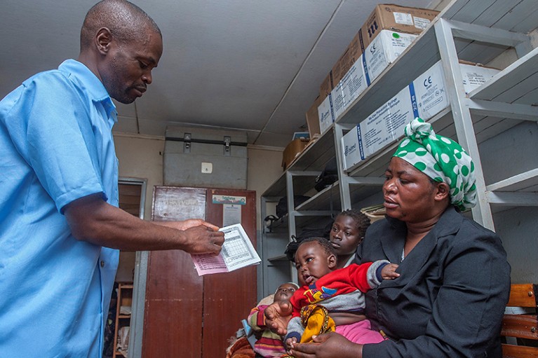 A health surveillance assistant shows a health passport for a mother and her child at a malaria-vaccine screening.