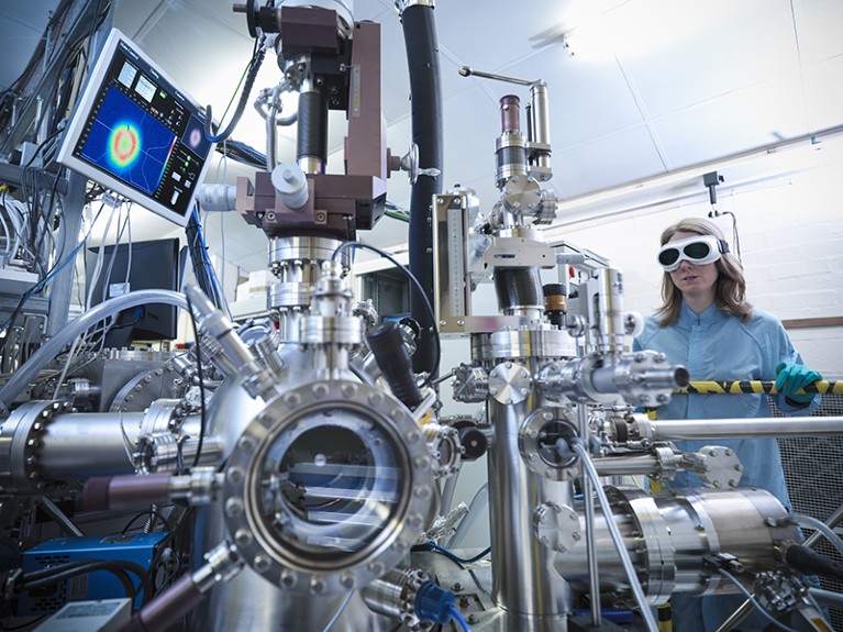 Female scientist using instrument in material science chamber.