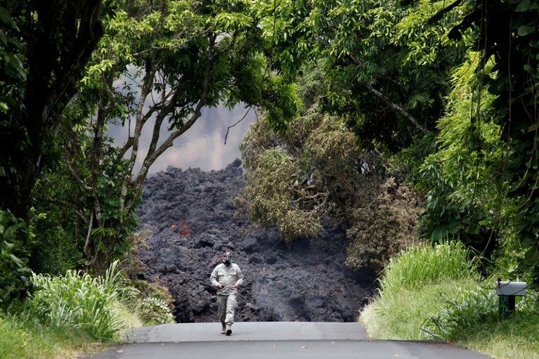 A figure in protective clothing walks on a road in front of the lava flow from the the Kilauea Volcano