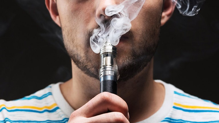 A young man exhales a cloud of vapour from an e-cigarette