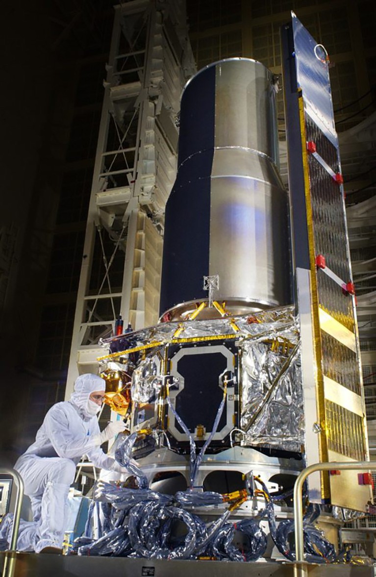 A person in a clean-suit works on satellite in a darkened facility