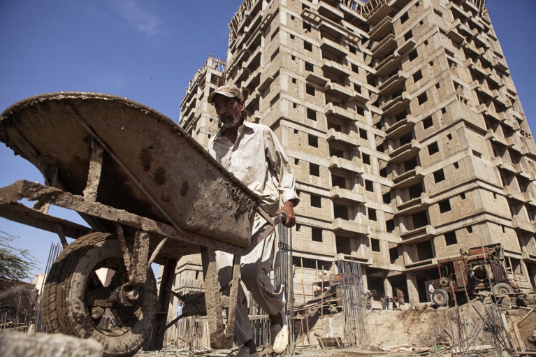 A laborer pushes a wheelbarrow load of concrete on the construction site in Karachi, Pakistan