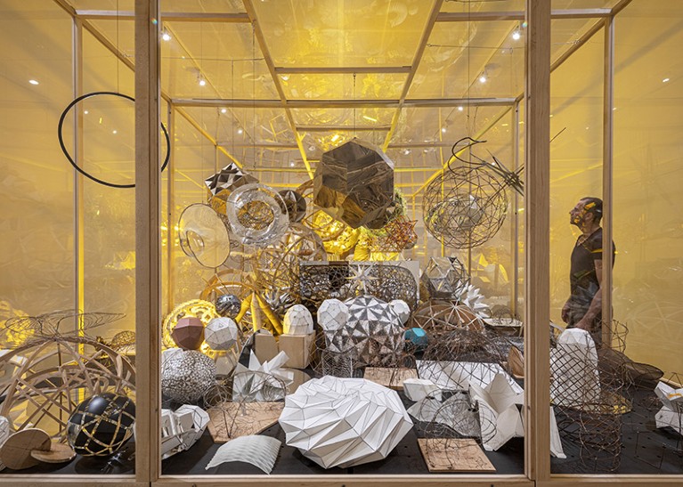 A glass case filled with models of various shapes made of paper, wire and other materials.