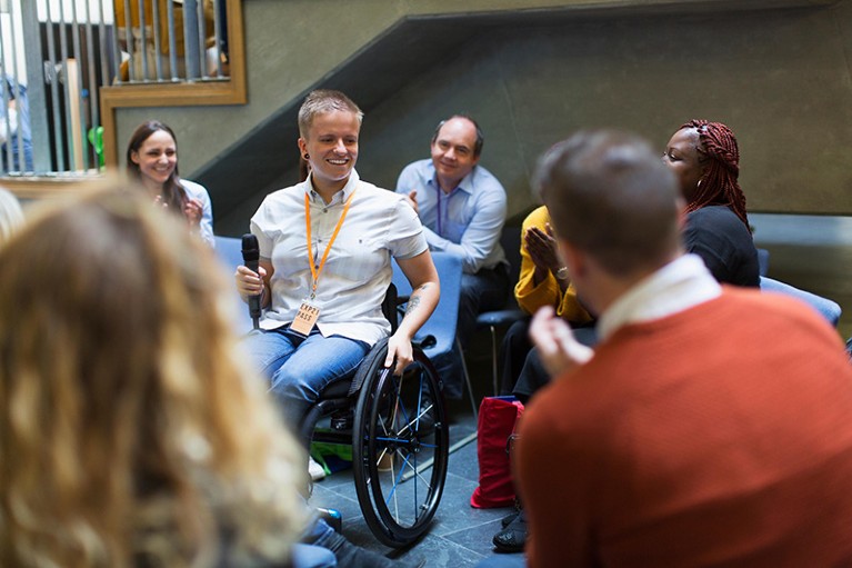 Photo of audience listening to female speaker with microphone in wheelchair