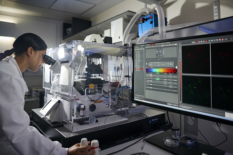 A researcher sits at a confocal microscope in a lab