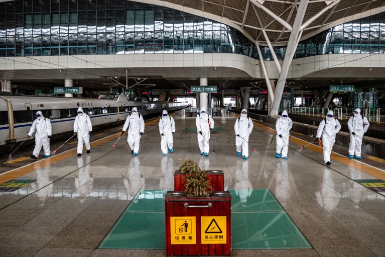 Staff members in protective clothing spray disinfectant at Wuhan Railway Station