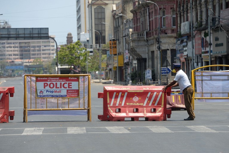 A policeman sets a barrier at a roadblock, India